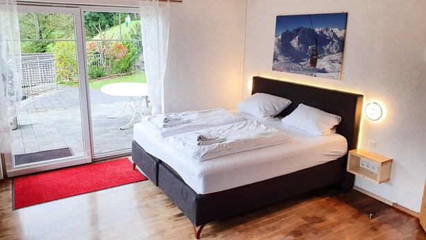 A bedroom with a bed, a nightstand, a wall-mounted light, and a window with a view of greenery. - Apartment for 6 persons Deluxe - Alpine jewel (Laimach)