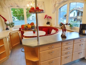 A kitchen with a central island, a dining area with a red sofa, and a view of houses through large windows.