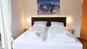 A hotel room with a bed, two bedside tables, a headboard, a window with curtains, and a wall-mounted picture of a mountain landscape. - Apartment for 6 persons Deluxe - Alpine jewel (Laimach)