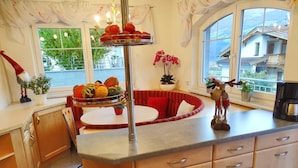 A kitchen with a central island, a dining area with a red sofa, and a view of houses through large windows. - Apartment for 6 persons Deluxe - Alpine jewel (Laimach)