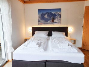 A hotel room with a bed, two bedside tables, a headboard, a window with curtains, and a wall-mounted picture of a mountain landscape. - Apartment for 6 persons Deluxe - Alpine jewel (Laimach)