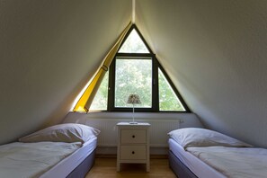 Una habitación con dos camas, una mesita de noche, una lámpara y un ventanal con vistas a árboles.