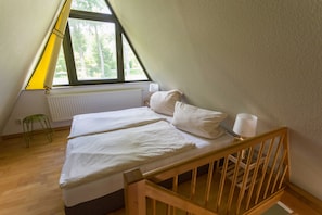Une petite pièce triangulaire comprenant un lit, une table de chevet, une lampe et un radiateur.