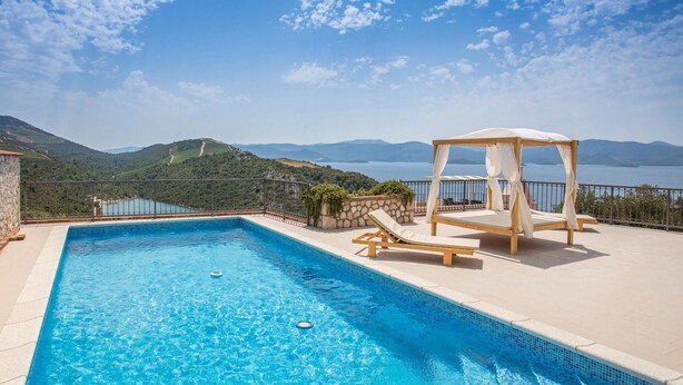 A clear blue swimming pool with a wooden deck, a wooden canopy, and a view of a lake and mountains. - Nice home in Kremena with sauna (Kremena)