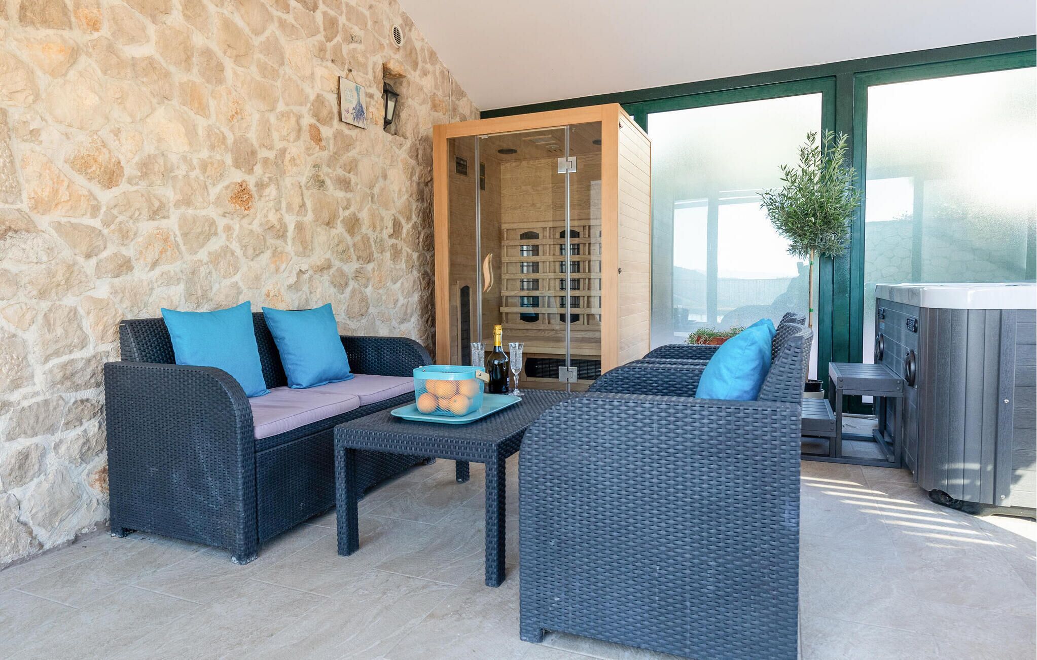 A modern outdoor seating area with wicker furniture, a stone wall, and a sauna.