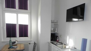 Une petite cuisine équipée avec une fenêtre, un évier, un four à micro-ondes et un téléviseur fixé au mur.