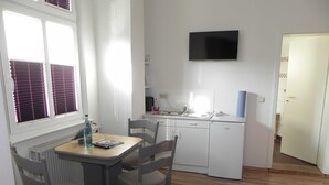 Une petite cuisine lumineuse, avec une table et des chaises, un four encastré et un téléviseur fixé au mur.