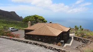 Un edificio de piedra con tejado de tejas, un camino de entrada pavimentado y vistas al mar.
