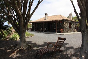 A stone building with a tiled roof, a bench, and a tree in the foreground.