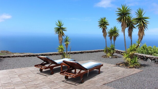 Terraza de madera con sillones de descanso y vista al océano.