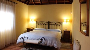Un dormitorio con una cama, mesitas de noche, un banco, un espejo y un radiador.