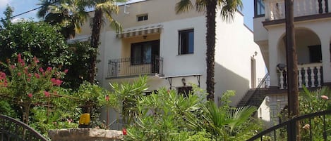 Un edificio de dos pisos con balcones, rodeado de palmeras y plantas en flor.
