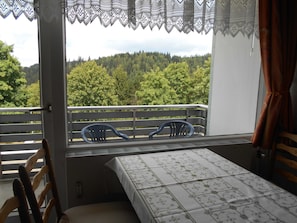 Un balcón con una mesa, sillas y vistas a un bosque.