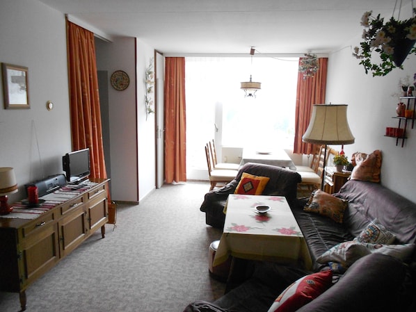 A living room with a sofa, a table, a television, and a dining area with chairs.
