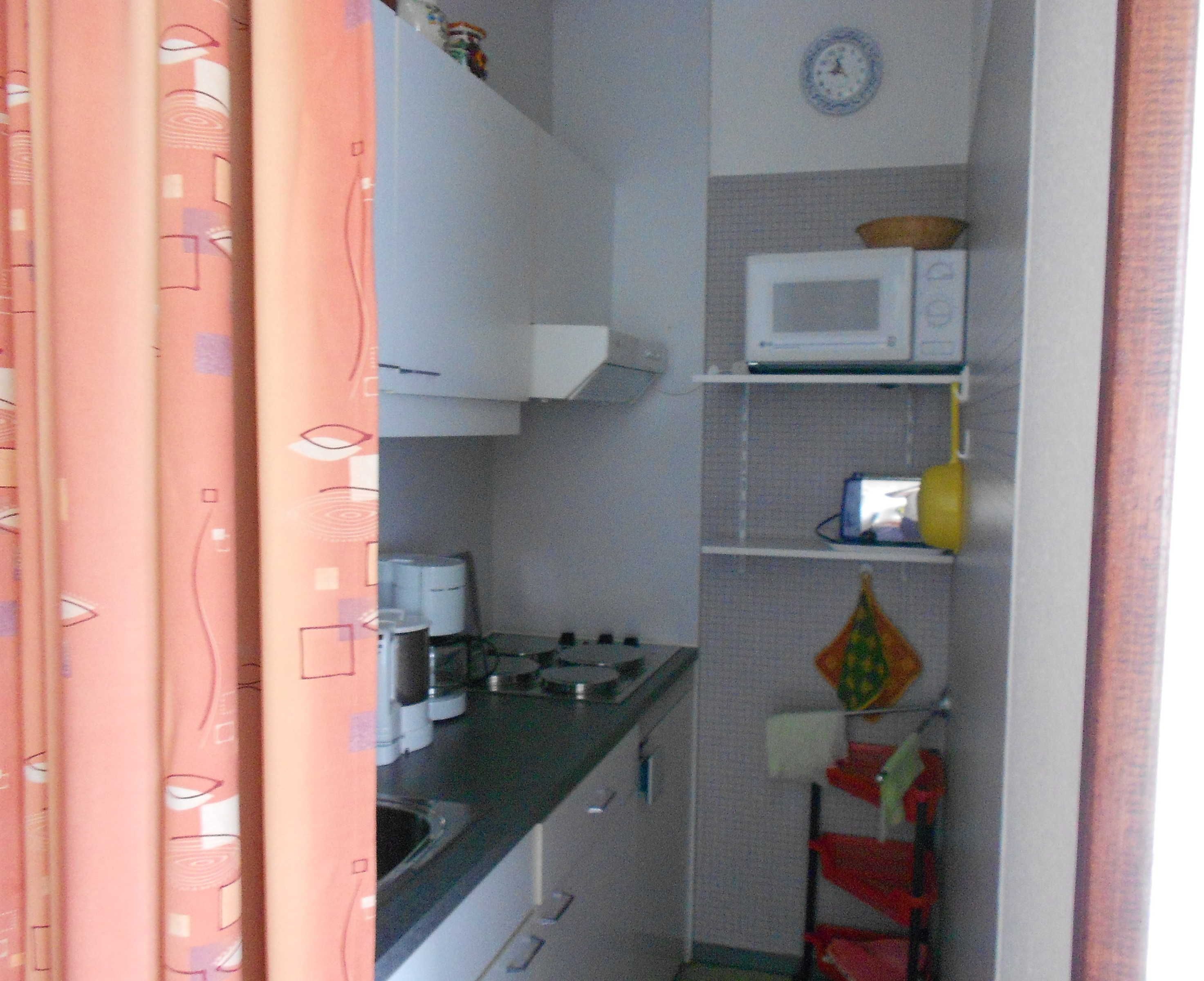 A compact kitchen with a microwave, stove, and a small shelf with a kettle and a yellow container.