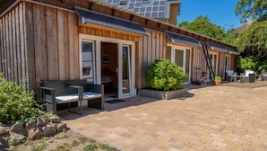 Ein Holzhaus mit Terrasse, Sitzgelegenheiten im Freien und einem kleinen Garten.