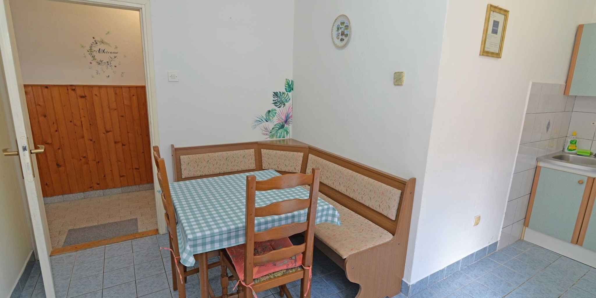 Una stanza piccola con una porta in legno, un tavolo a scacchi, un letto angolare, un decoro a parete e un angolo cottura.