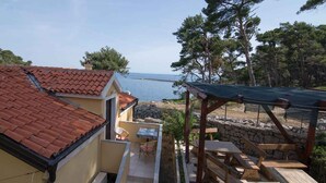 A coastal property with a tiled roof, a patio with a table and chairs, and a view of the sea. - Holiday apartment with terrace (Veli Lošinj)