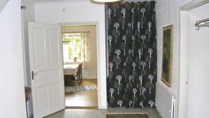 A hallway with a white door, a dining area with a table and chairs, and a black curtain with a tree pattern.