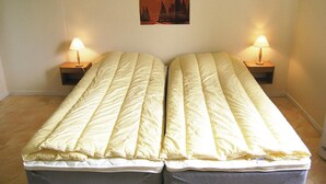 A twin bed with a quilted duvet, two bedside tables with lamps, and a painting of sailboats on the wall.