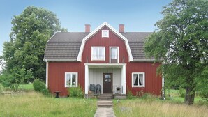 A red house with a front porch, a chimney, and a pathway leading to the entrance.