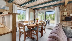 A cozy room with wooden walls and ceiling, a dining table with chairs, a sofa, and a TV on a wooden shelf. - 3 bedroom cozy home in Rømø (Rømø)
