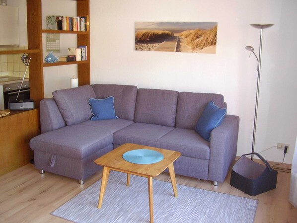 A living room with a purple sectional sofa, a wooden coffee table, a bookshelf, a painting, and a floor lamp.