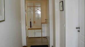 A hallway with a wooden floor, a black doormat, a coat rack with hangers, and a door with a picture frame.