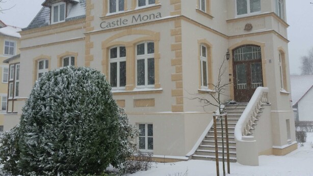 A large, historic building labeled 'Castle Mona' with a prominent entrance and a staircase leading to the main entrance.
