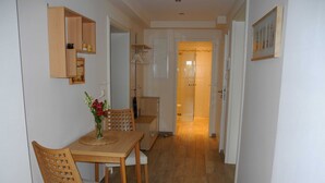 A hallway with a wooden dining table and chairs, a vase with flowers, a wooden cabinet, and a bathroom visible in the background.