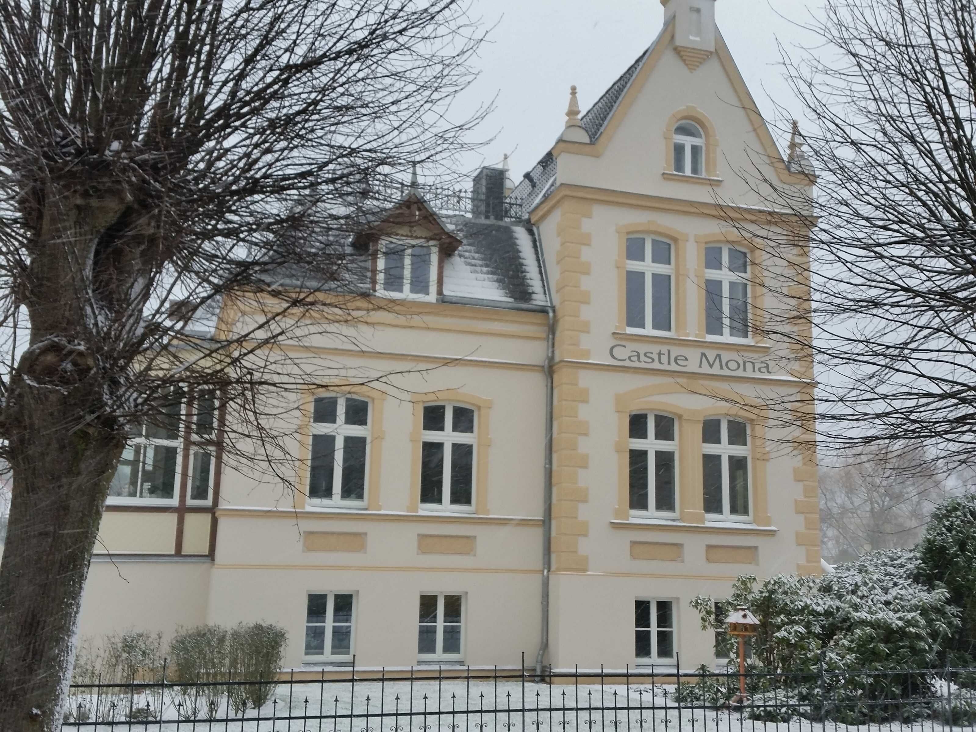 Un edificio con el letrero 'Castle Mona', de estilo arquitectónico tradicional, con varias ventanas y una torre destacada.