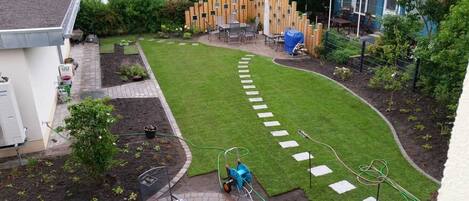 A garden with a lawn, stepping stones, a wooden fence, and a patio area with outdoor furniture.