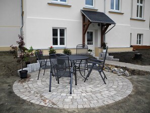 Eine Terrasse mit einem runden Tisch und Stühlen, umgeben von Kübelpflanzen.