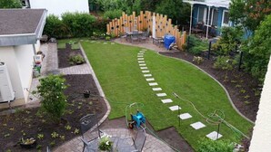 A garden with a lawn, stepping stones, a wooden fence, and a patio area with outdoor furniture.