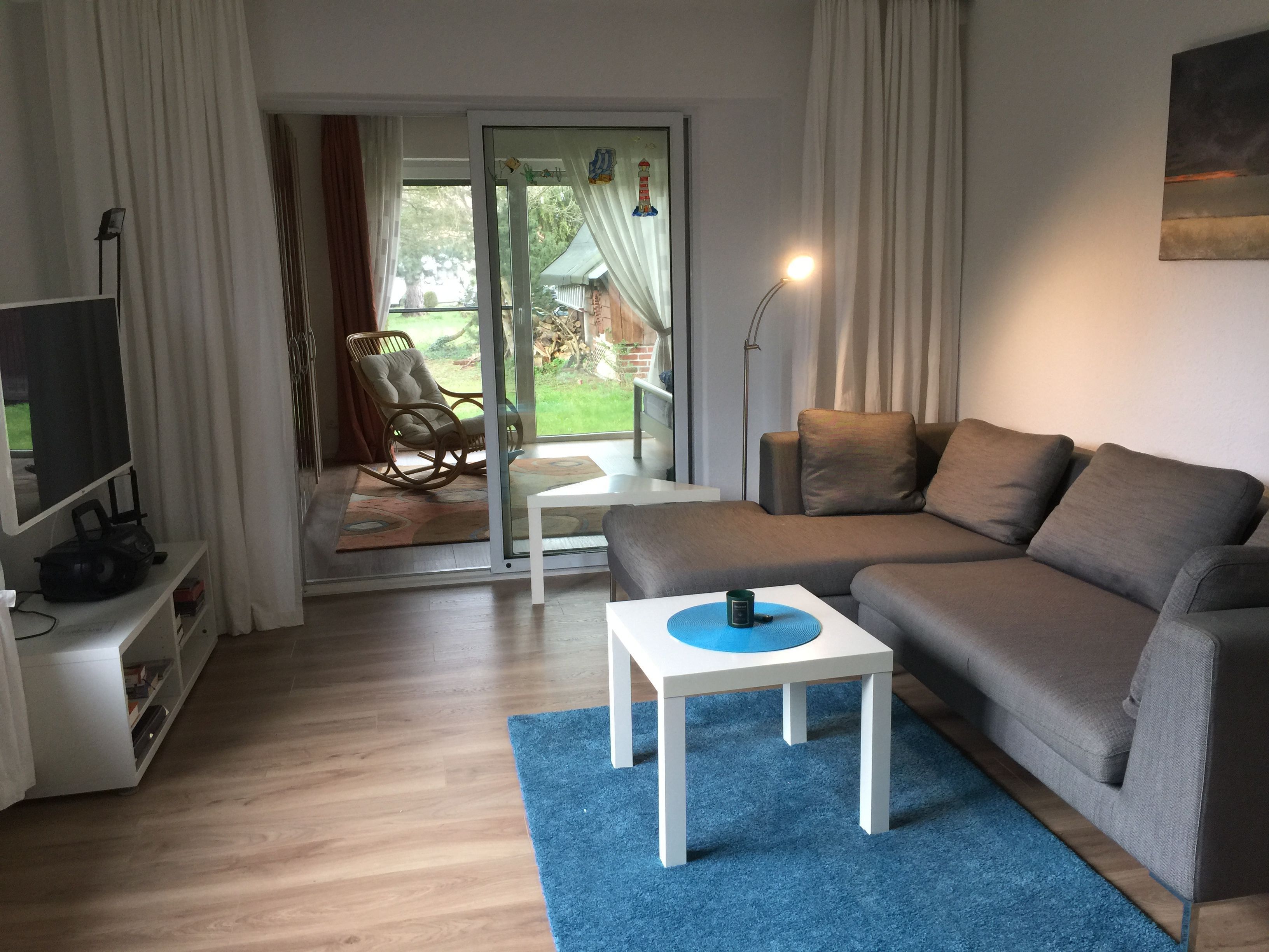 En moderne stue med sofa, et lille bord, et fjernsyn og en skydedør, der fører ud til en terrasse.
