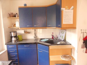 A compact kitchen with blue cabinets, a coffee maker, a sink, and a small shelf with kitchen utensils. - Schiel apartment rental - Apartment (Zempin)