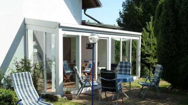 A covered patio with a table and chairs, a striped lounge chair, and a view of the interior through glass doors. - Schiel apartment rental - Apartment (Zempin)