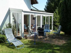 A covered patio with a table and chairs, a striped lounge chair, and a view of the interior through glass doors. - Schiel apartment rental - Apartment (Zempin)
