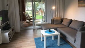 A modern living room with a sofa, a small table, a TV, and a sliding glass door leading to a patio. - Schiel apartment rental - Apartment (Zempin)