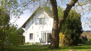 A house with a large tree in the front yard, a patio with chairs, and a clear sky. - Schiel apartment rental - Apartment (Zempin)