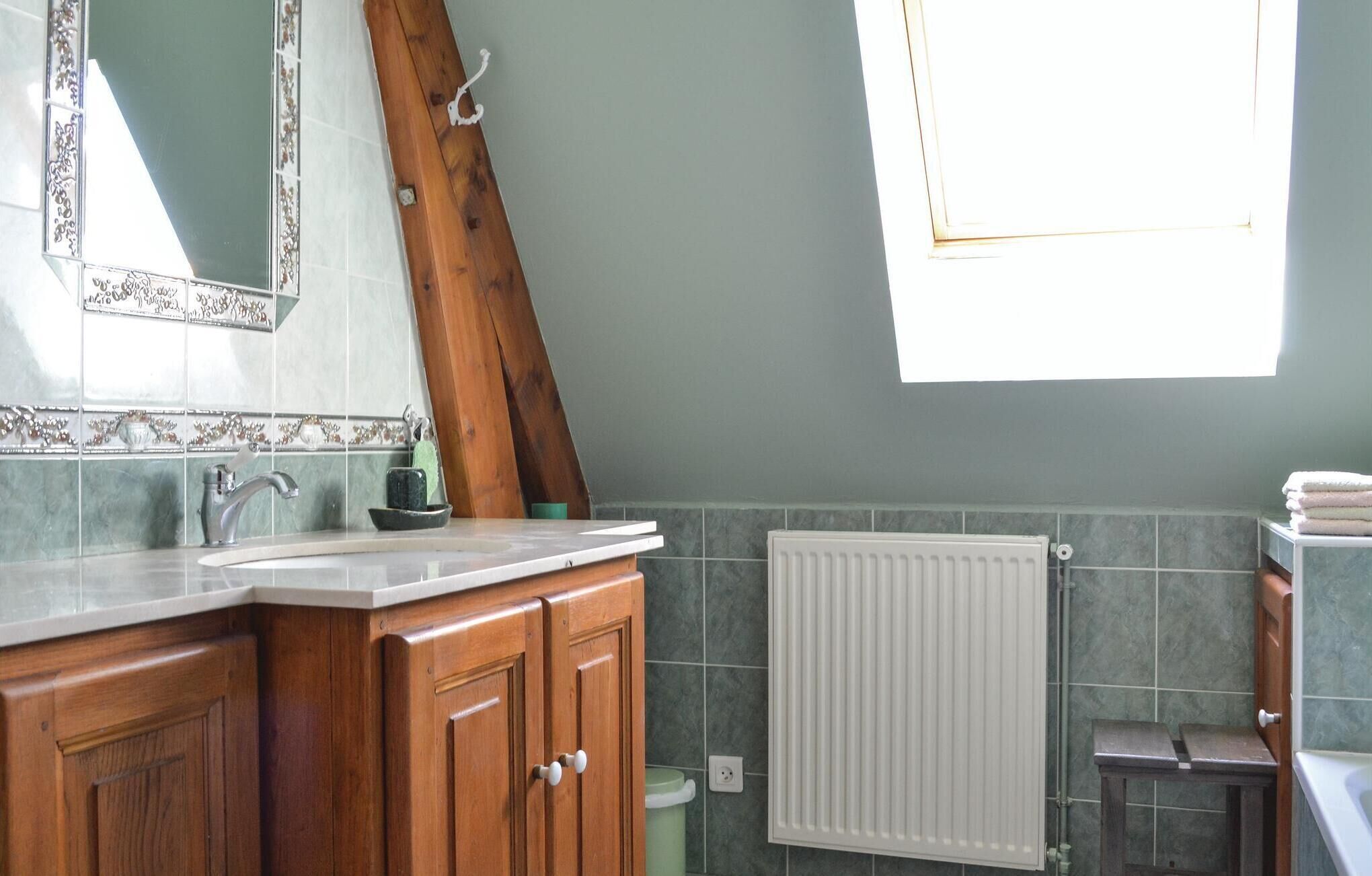 A bathroom with a wooden vanity, a mirror with decorative tiles, a radiator, and a window providing natural light.