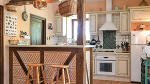 Una cucina con isola centrale, sgabelli in legno, piano cottura a gas, mobili bianchi e schienale piastrellato.