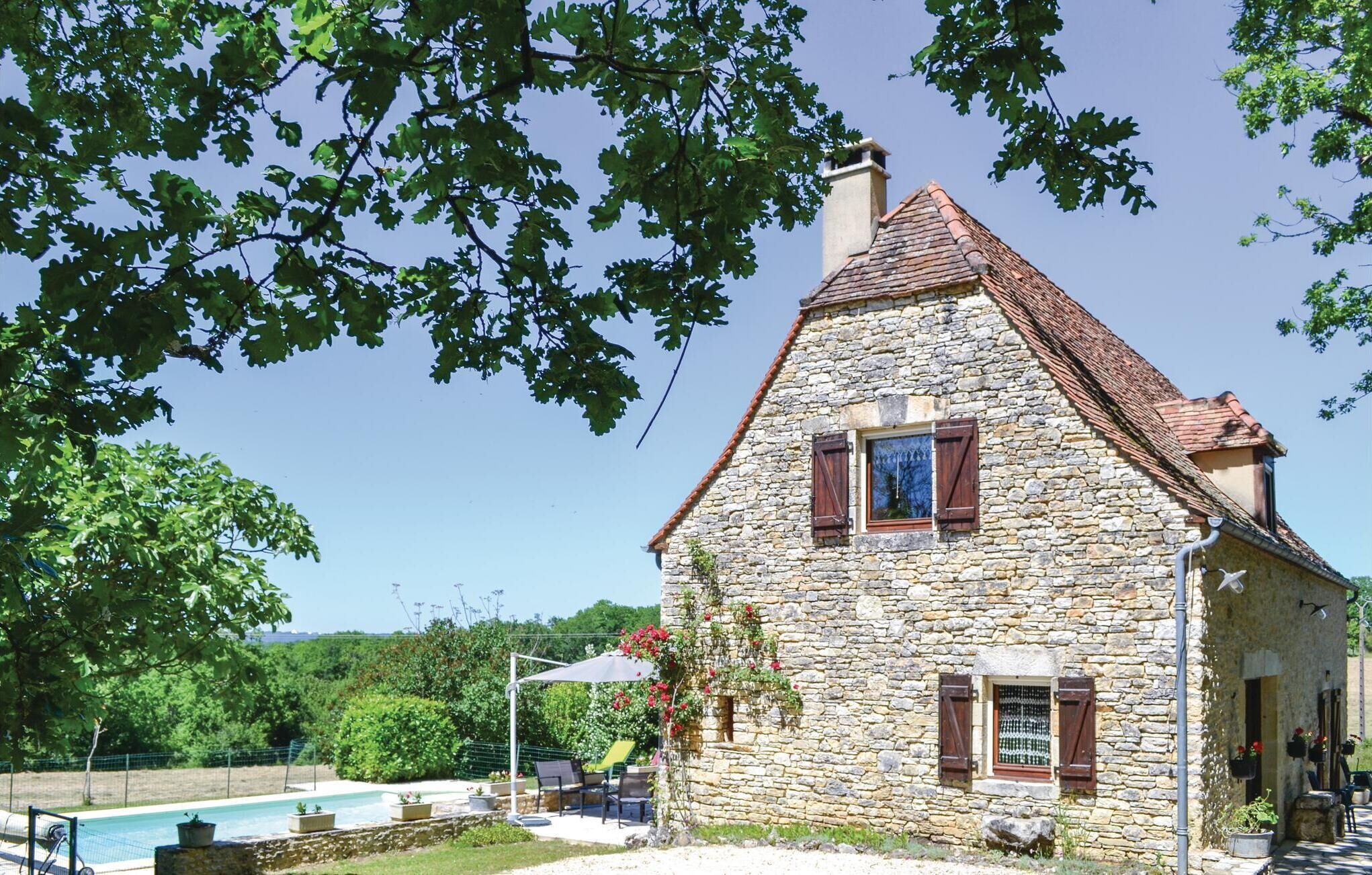 Una casa de piedra con techo de tejas, piscina y mobiliario exterior.