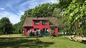 A red house with a green lawn and a tree in the foreground. - Vacation apartment Möwe (ground floor) - Windland Ranch - Equestrian farm with vacation apartments (House (Altenkirchen)
