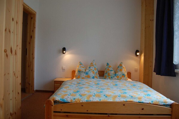 Ein hölzernes Bett mit floraler Bettdecke, zwei Wandlampen und eine Holztür.