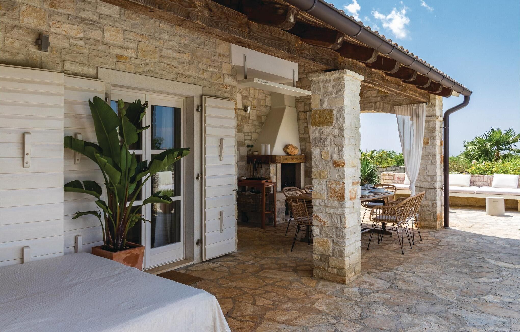 Un edificio de piedra con un porche cubierto, chimenea y mobiliario exterior.