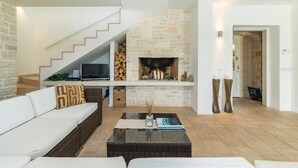 A modern living room with a stone fireplace, a white staircase, and a flat-screen TV on a white console table.