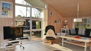 Ein modernes Wohnzimmer mit Fernseher, einer bequemen Couch, einem Esstisch und einem großen Fenster mit Blick ins Freie.