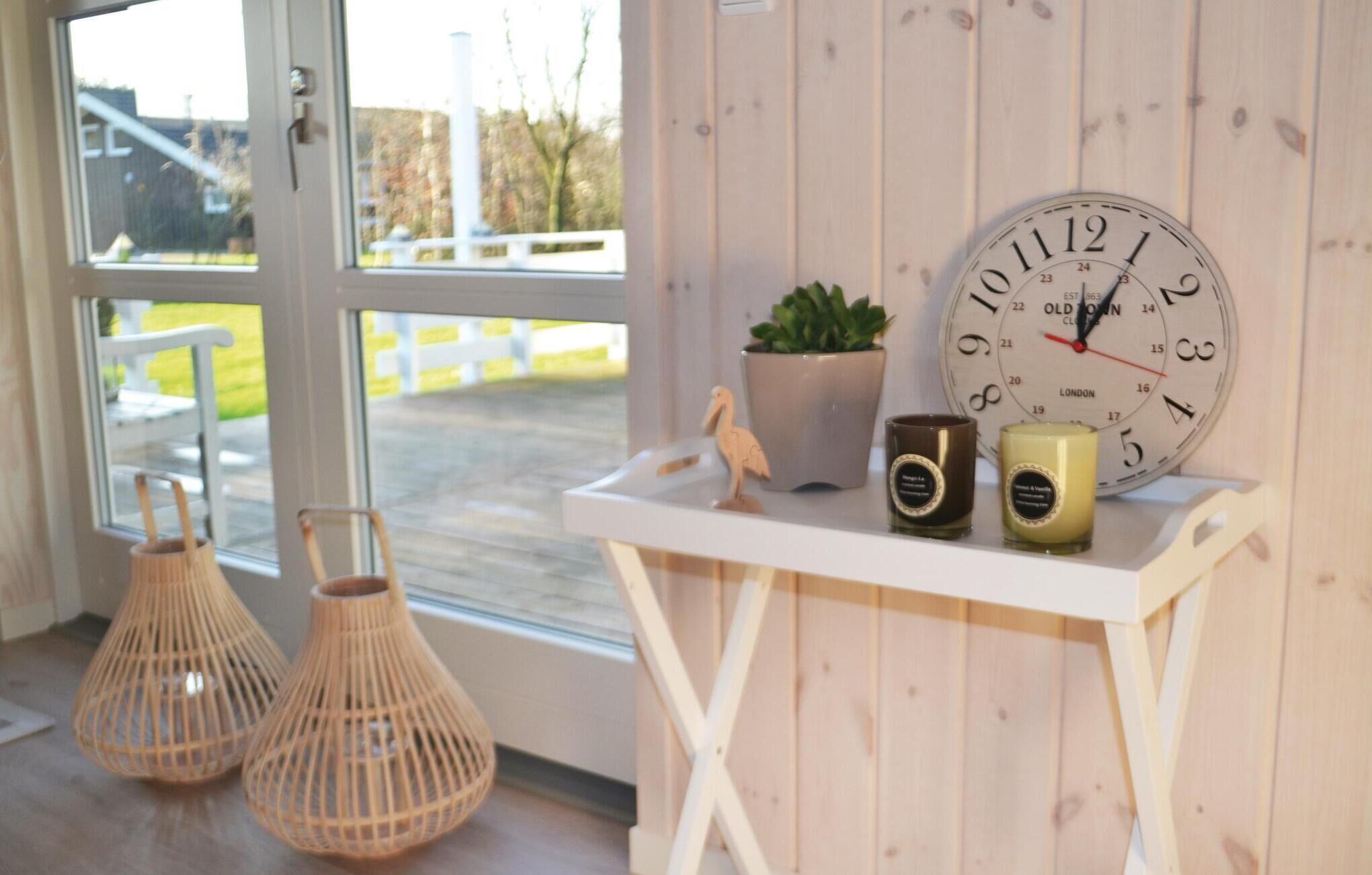 Une pièce avec un mur en bois, une table blanche ornée d’une horloge, de bougies et d’une plante en pot.