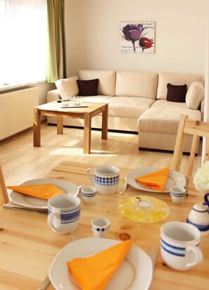 A cozy living room with a sofa, a wooden coffee table, and a dining area with plates, cups, and a napkin.